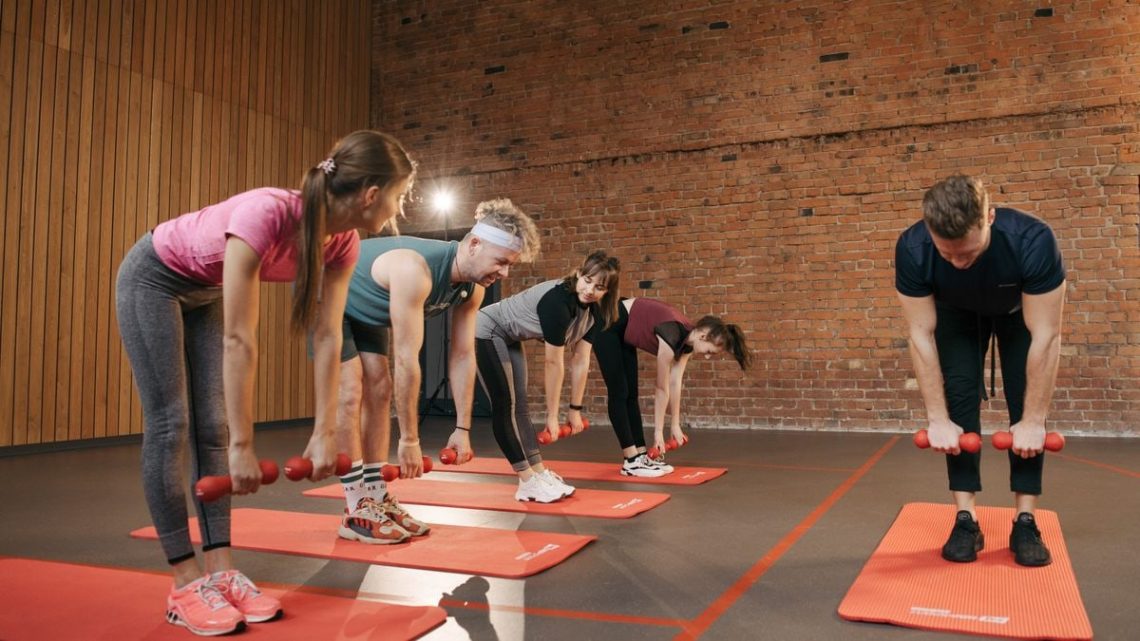 Fitness group performing exercises with dumbbells in a modern yoga studio setting.