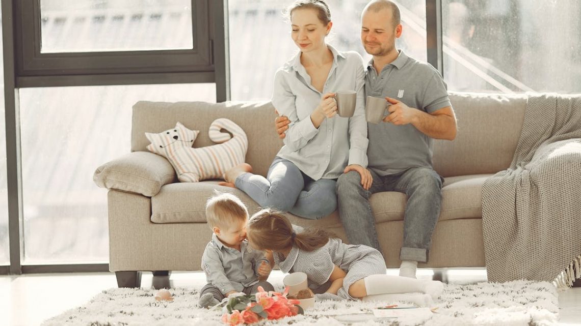 Cheerful family smiling while spending weekend together sitting parents sitting on comfortable sofa while children resting on carpet and playing