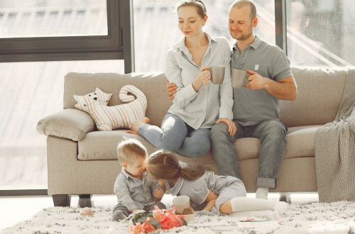 Cheerful family smiling while spending weekend together sitting parents sitting on comfortable sofa while children resting on carpet and playing
